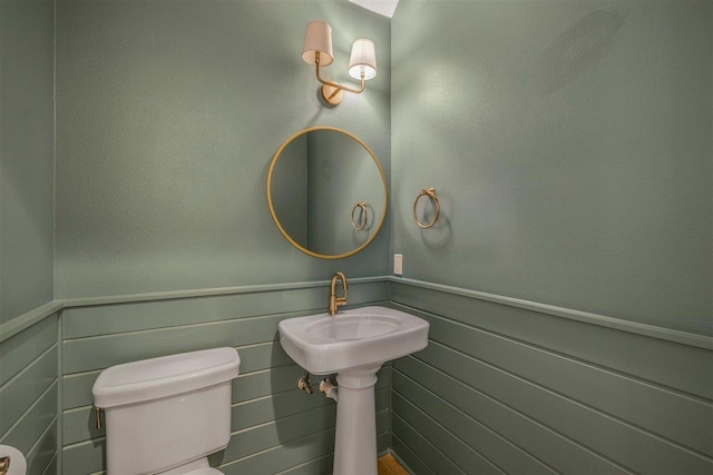 half bath featuring a wainscoted wall, a sink, and toilet