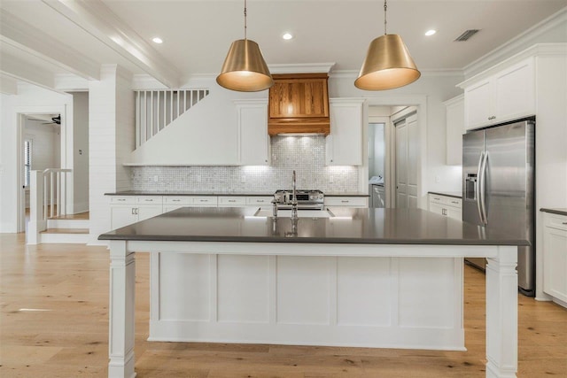 kitchen with light wood finished floors, visible vents, stainless steel fridge with ice dispenser, dark countertops, and ornamental molding