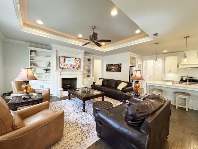 living room with crown molding, a raised ceiling, dark wood-style flooring, and ceiling fan