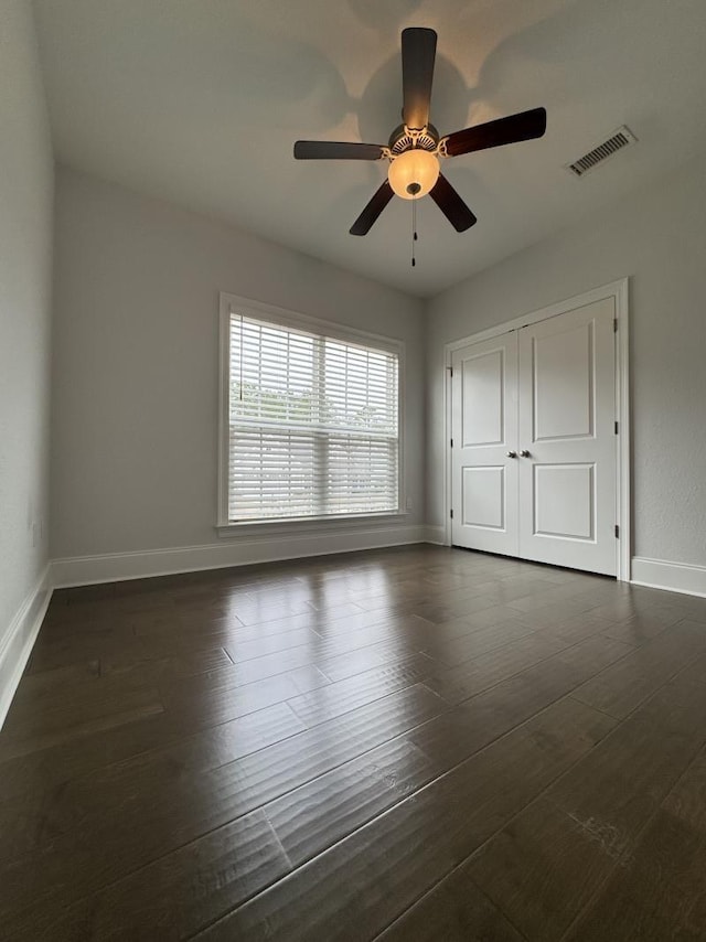 unfurnished bedroom with visible vents, a closet, baseboards, ceiling fan, and dark wood-type flooring