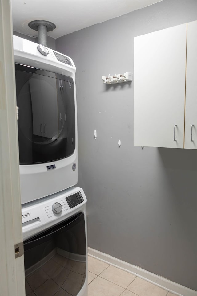 laundry area with stacked washer and dryer, light tile patterned floors, and cabinets