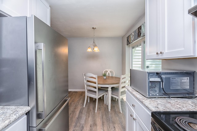 kitchen featuring light stone countertops, pendant lighting, a chandelier, white cabinetry, and stainless steel refrigerator