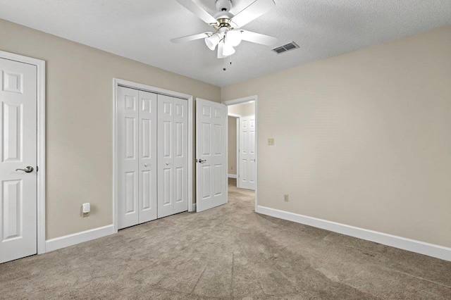 unfurnished bedroom featuring ceiling fan, light colored carpet, a closet, and a textured ceiling