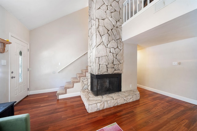 interior space with baseboards, wood finished floors, stairs, a stone fireplace, and high vaulted ceiling