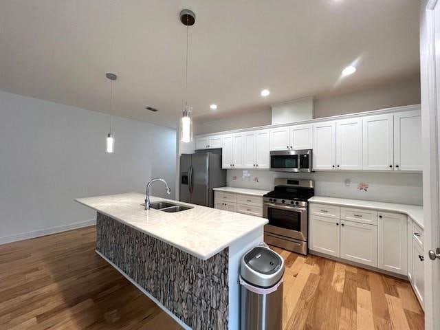 kitchen with white cabinetry, sink, appliances with stainless steel finishes, decorative light fixtures, and light wood-type flooring