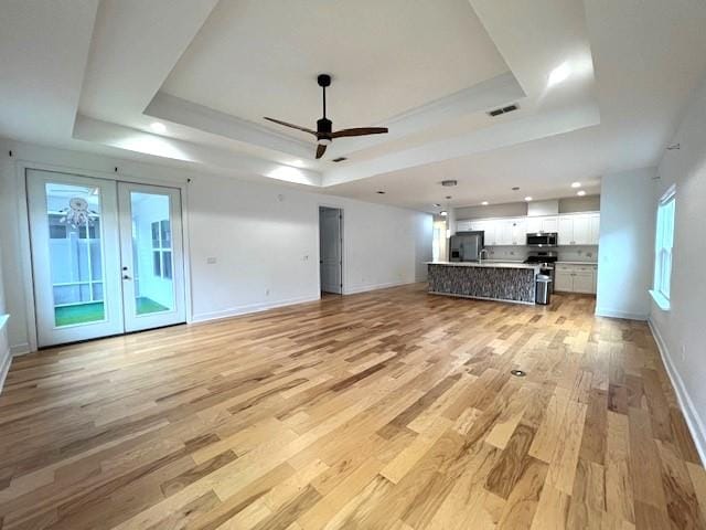 unfurnished living room featuring french doors, light hardwood / wood-style floors, ceiling fan, and a tray ceiling