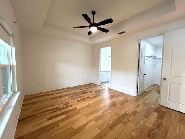 unfurnished room with ceiling fan, light wood-type flooring, and a tray ceiling