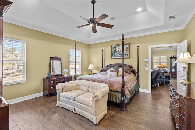 bedroom featuring dark hardwood / wood-style floors, multiple windows, ornamental molding, ceiling fan, and a tray ceiling