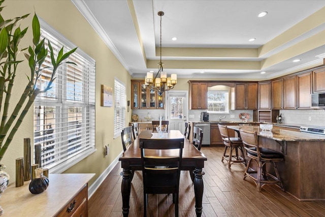 dining room with an inviting chandelier, ornamental molding, dark hardwood / wood-style floors, and a raised ceiling