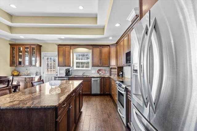 kitchen with stainless steel appliances, a raised ceiling, dark stone countertops, and backsplash