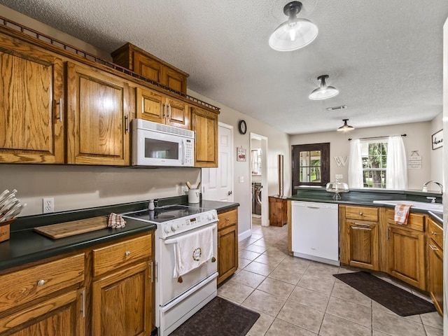 kitchen with light tile patterned flooring, white appliances, kitchen peninsula, washing machine and dryer, and a textured ceiling