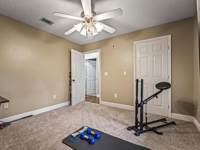 exercise room featuring ceiling fan, carpet floors, and a textured ceiling