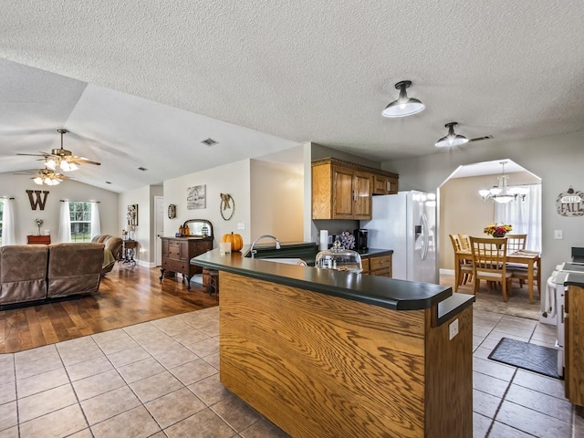 kitchen with light tile patterned flooring, white refrigerator with ice dispenser, ceiling fan with notable chandelier, and kitchen peninsula