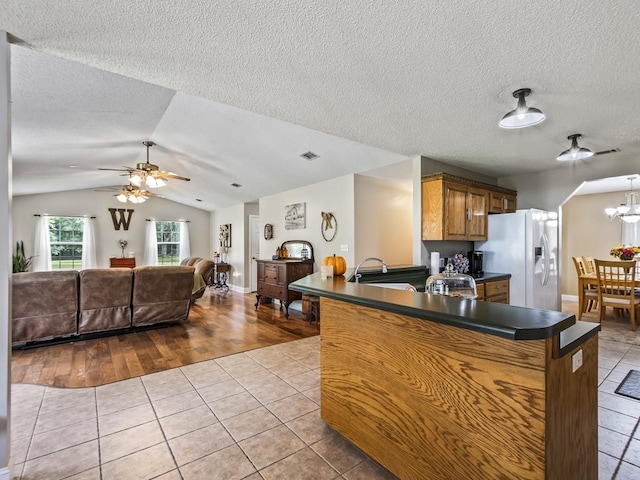 kitchen featuring lofted ceiling, kitchen peninsula, light tile patterned floors, and white fridge with ice dispenser