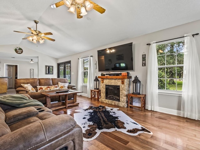 living room with hardwood / wood-style flooring, vaulted ceiling, a stone fireplace, and ceiling fan