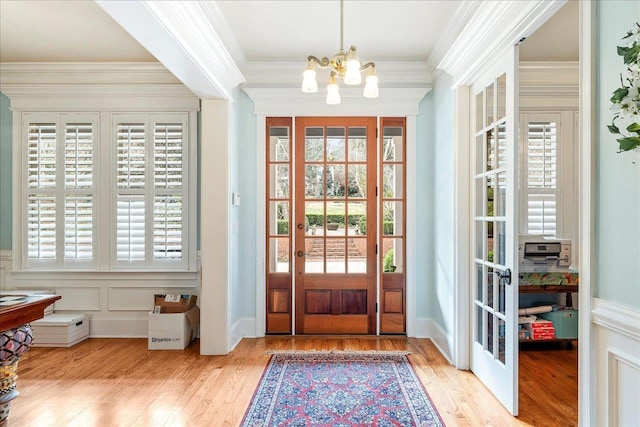 entryway with crown molding, light hardwood / wood-style floors, french doors, and a notable chandelier