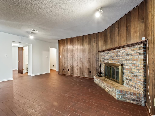 unfurnished living room with wooden walls, a fireplace, dark hardwood / wood-style flooring, and a textured ceiling