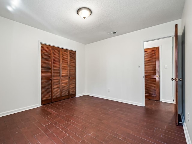 unfurnished bedroom featuring a textured ceiling, dark hardwood / wood-style flooring, and a closet