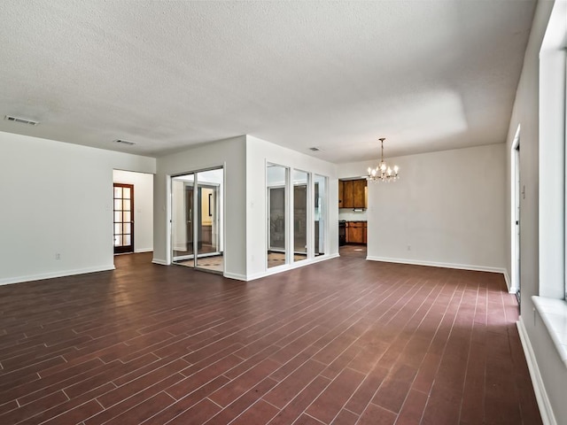 unfurnished living room featuring a notable chandelier, dark wood-type flooring, and a textured ceiling