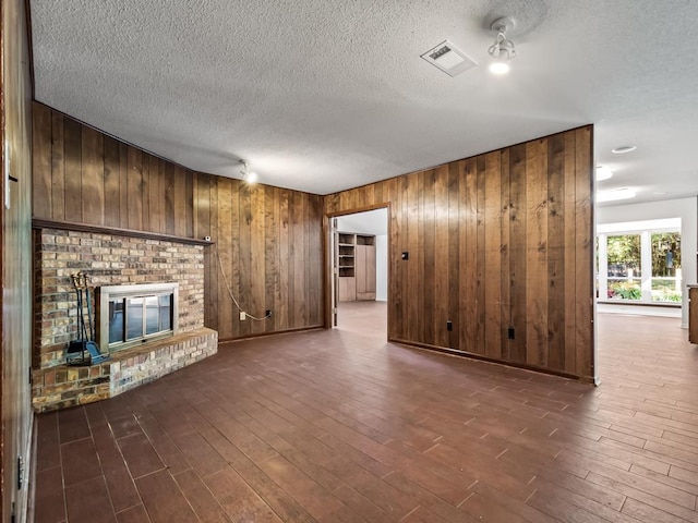 unfurnished living room with a brick fireplace, wooden walls, a textured ceiling, and dark hardwood / wood-style flooring