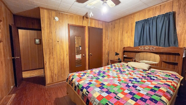 bedroom featuring ceiling fan, dark hardwood / wood-style floors, and wood walls