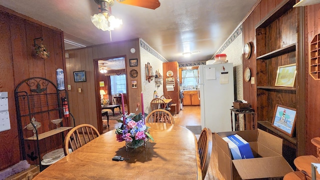 dining space with ceiling fan and wood walls