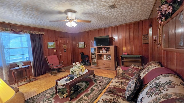 living room featuring a textured ceiling, light parquet floors, wood walls, and ceiling fan