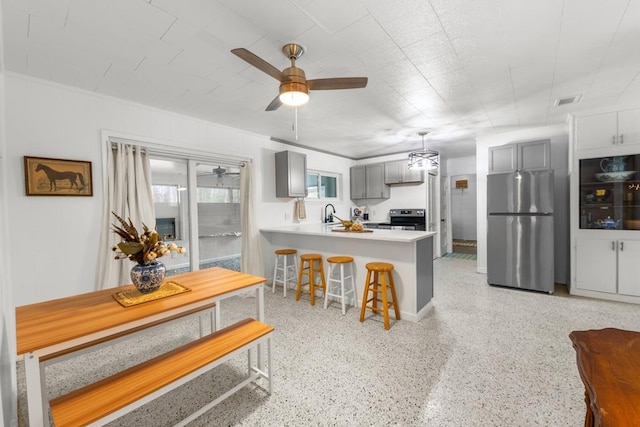 kitchen with appliances with stainless steel finishes, gray cabinets, kitchen peninsula, ceiling fan, and a breakfast bar area