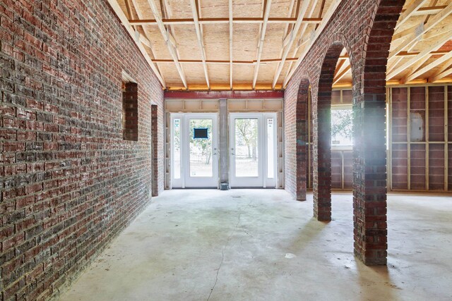 miscellaneous room with plenty of natural light, brick wall, decorative columns, and concrete floors