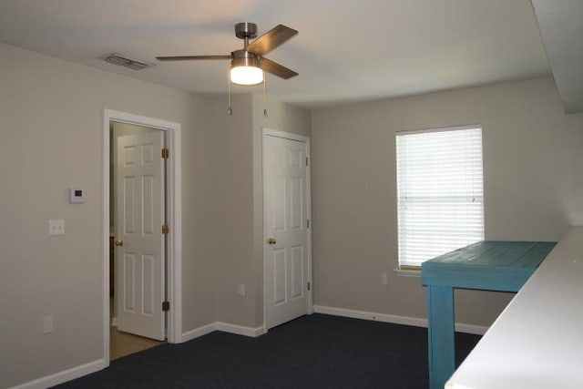 interior space featuring multiple windows, dark carpet, and ceiling fan