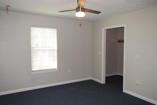 unfurnished bedroom with dark carpet, a closet, ceiling fan, and a spacious closet