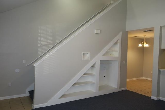 stairway with tile patterned floors, built in features, and a chandelier