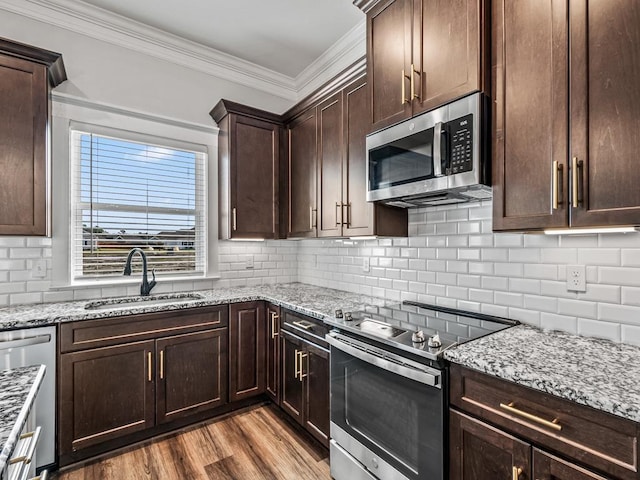 kitchen featuring crown molding, appliances with stainless steel finishes, a sink, dark brown cabinets, and light stone countertops