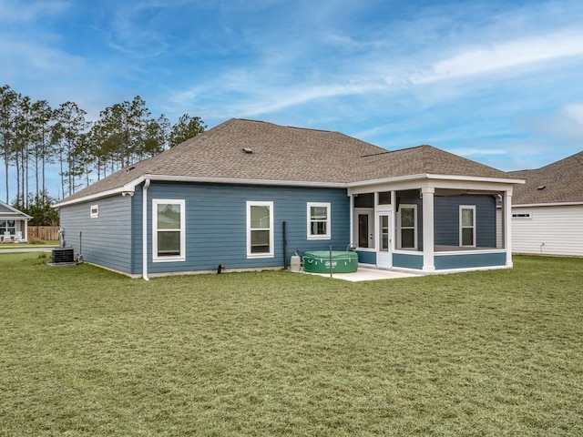 rear view of house with central air condition unit, a sunroom, a lawn, roof with shingles, and a patio area