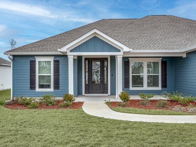 view of exterior entry with board and batten siding, a shingled roof, and a lawn