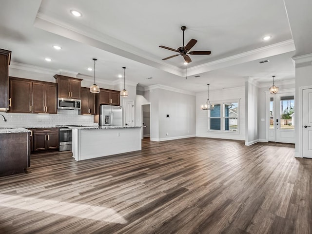 kitchen with stainless steel appliances, a kitchen island, open floor plan, light stone countertops, and a tray ceiling