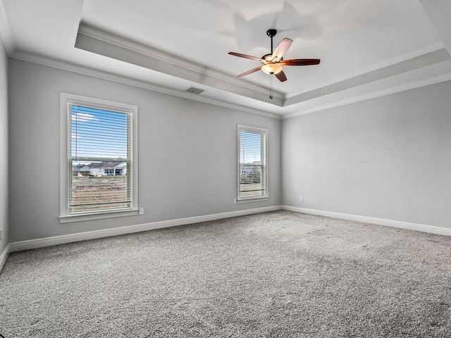 carpeted empty room featuring ornamental molding, a tray ceiling, visible vents, and baseboards