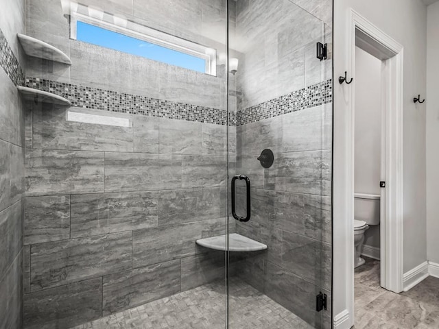 bathroom featuring toilet, a stall shower, and baseboards