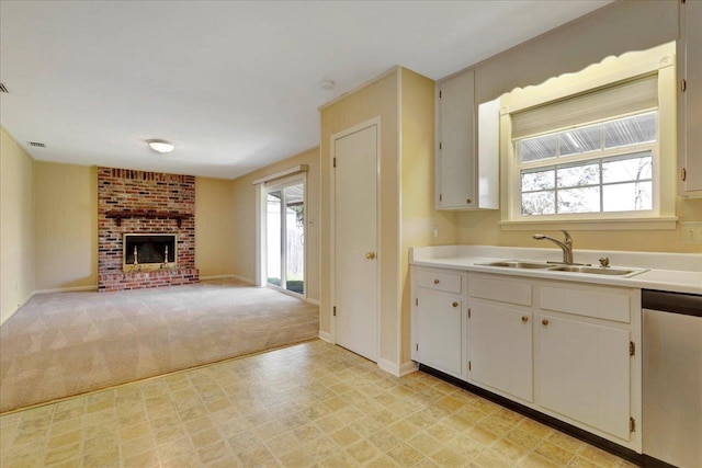 kitchen with light carpet, a sink, light countertops, a brick fireplace, and dishwasher