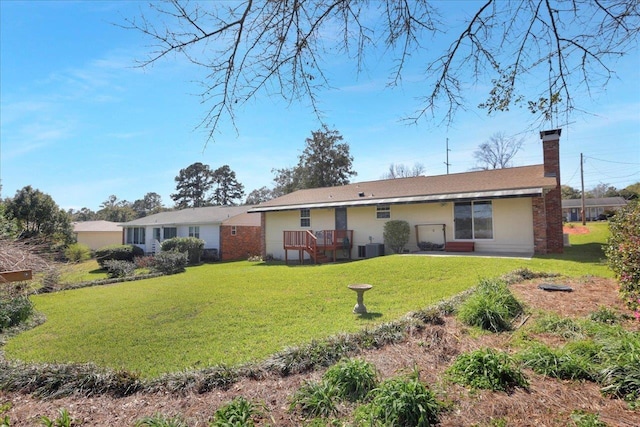 rear view of property with a yard, central AC unit, a chimney, and stucco siding