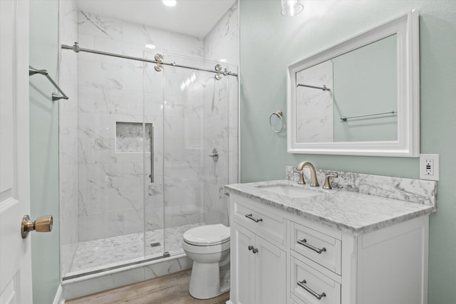 full bathroom with vanity, toilet, a marble finish shower, and wood finished floors