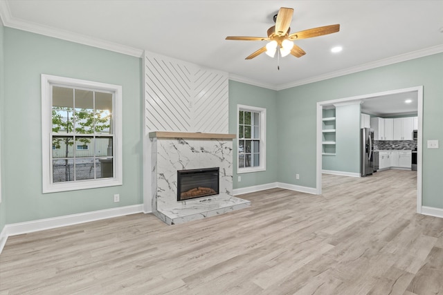 unfurnished living room with light wood-style flooring, a ceiling fan, baseboards, a high end fireplace, and ornamental molding