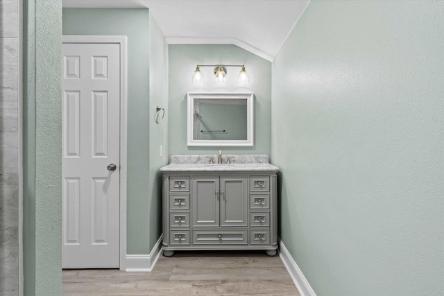 bathroom with vanity, baseboards, lofted ceiling, and wood finished floors