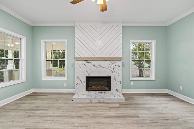 unfurnished living room featuring a high end fireplace, ornamental molding, a ceiling fan, and wood finished floors