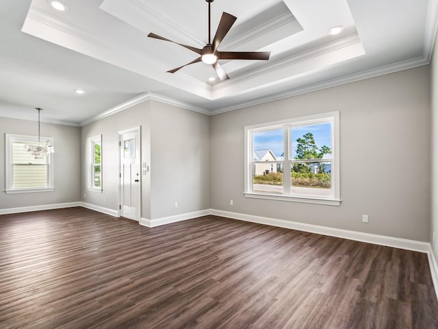 empty room with ornamental molding, ceiling fan with notable chandelier, dark hardwood / wood-style flooring, and a raised ceiling