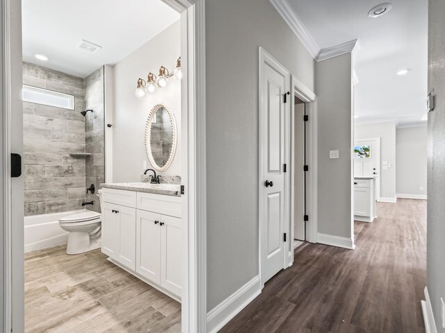 full bathroom with toilet, tiled shower / bath, hardwood / wood-style flooring, ornamental molding, and vanity