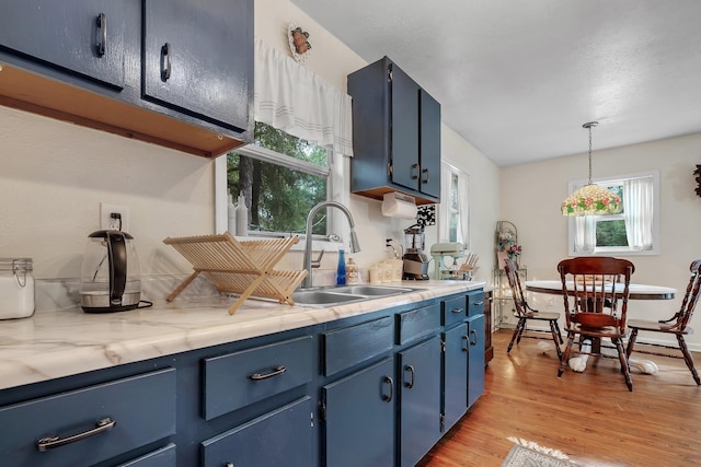 kitchen featuring blue cabinets, sink, hanging light fixtures, and light wood-type flooring