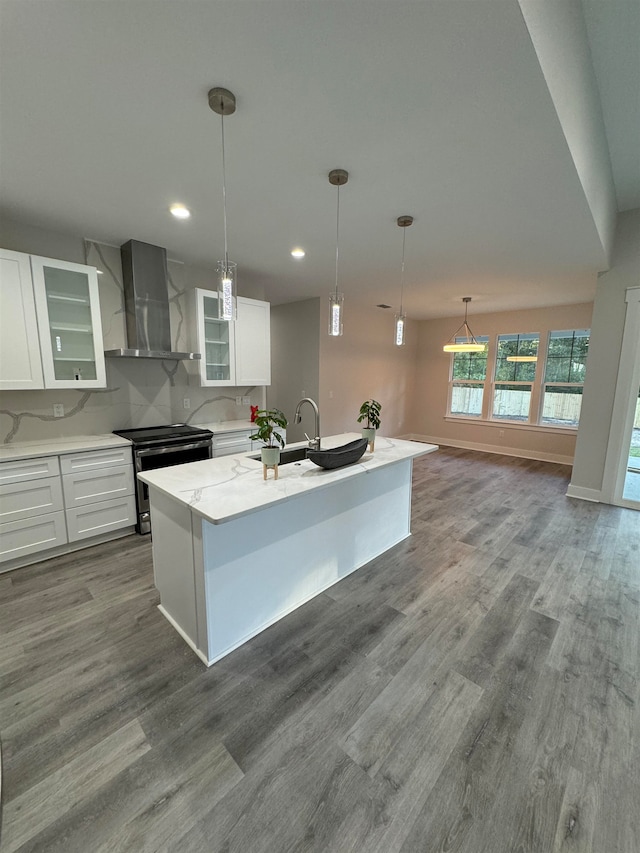 kitchen with stainless steel range with electric cooktop, wall chimney exhaust hood, an island with sink, white cabinetry, and wood-type flooring