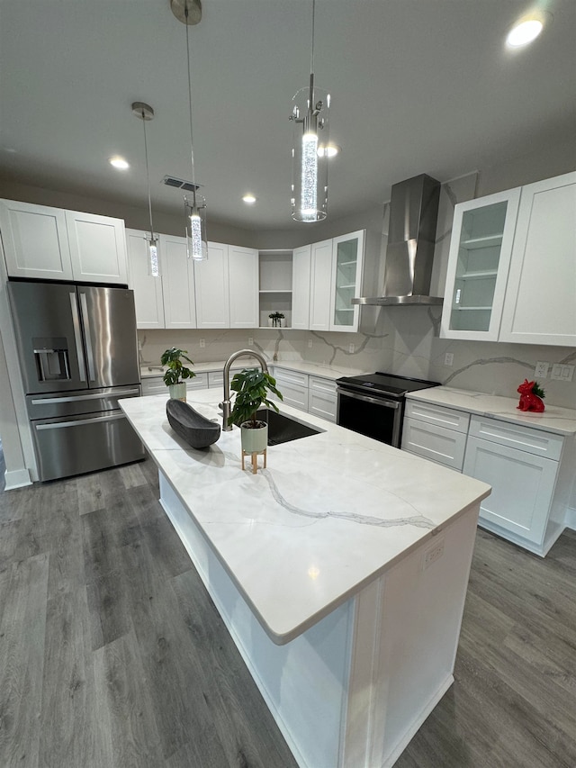 kitchen featuring white cabinets, an island with sink, wall chimney range hood, and appliances with stainless steel finishes