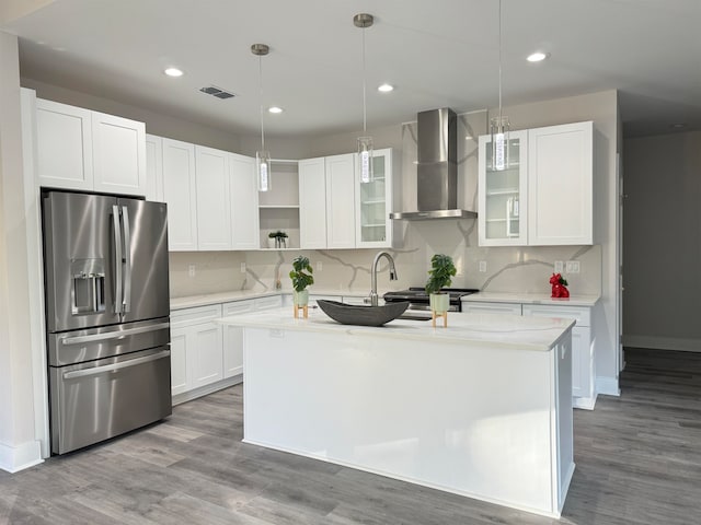 kitchen with wall chimney range hood, appliances with stainless steel finishes, pendant lighting, white cabinets, and hardwood / wood-style flooring